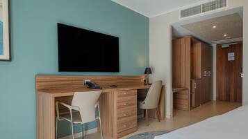 A hotel room with a bed, a desk with a chair, a television, a wardrobe, and a bathroom.