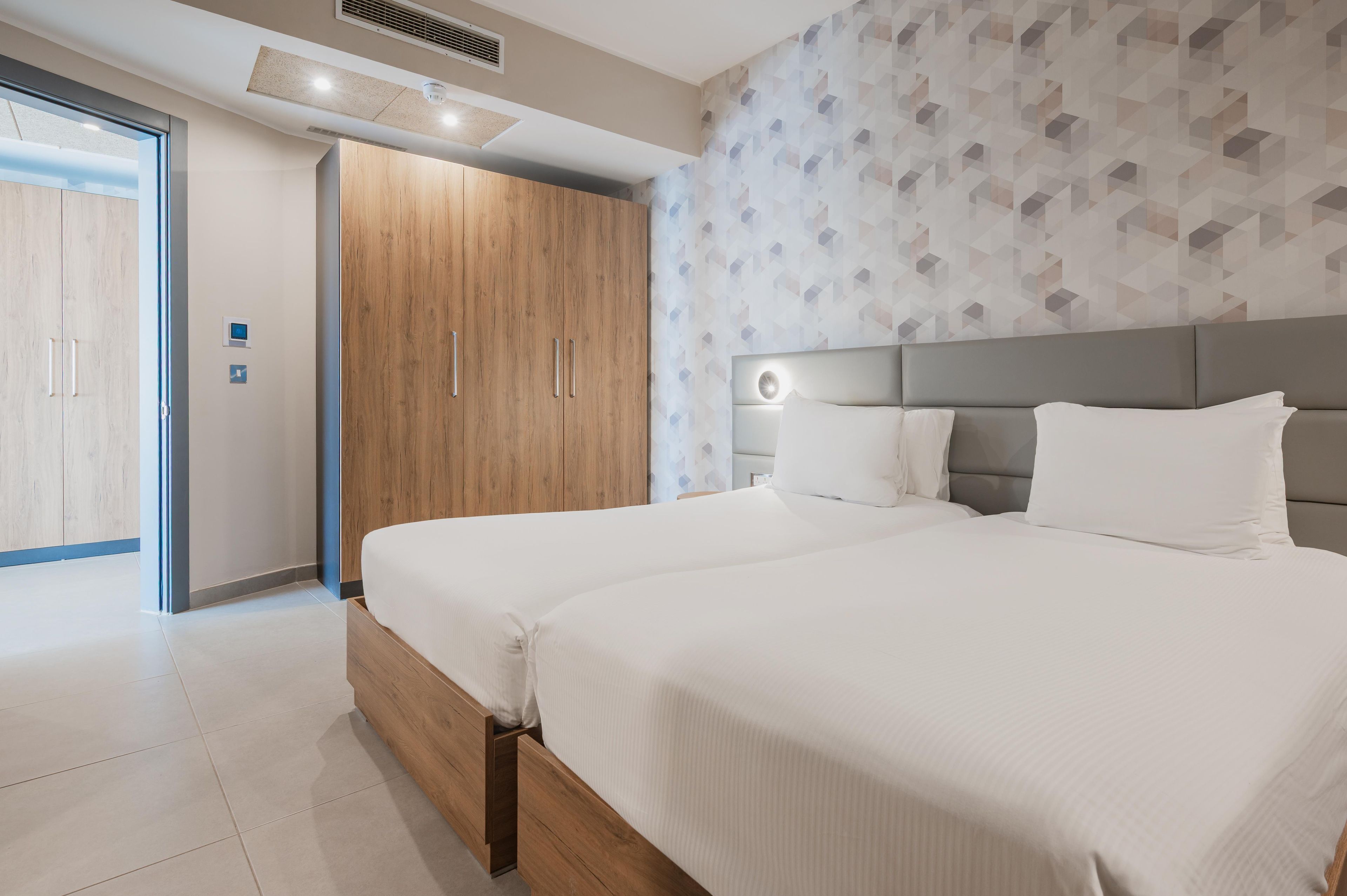 A modern hotel room with a large bed, a wardrobe, and a geometric-patterned wall.