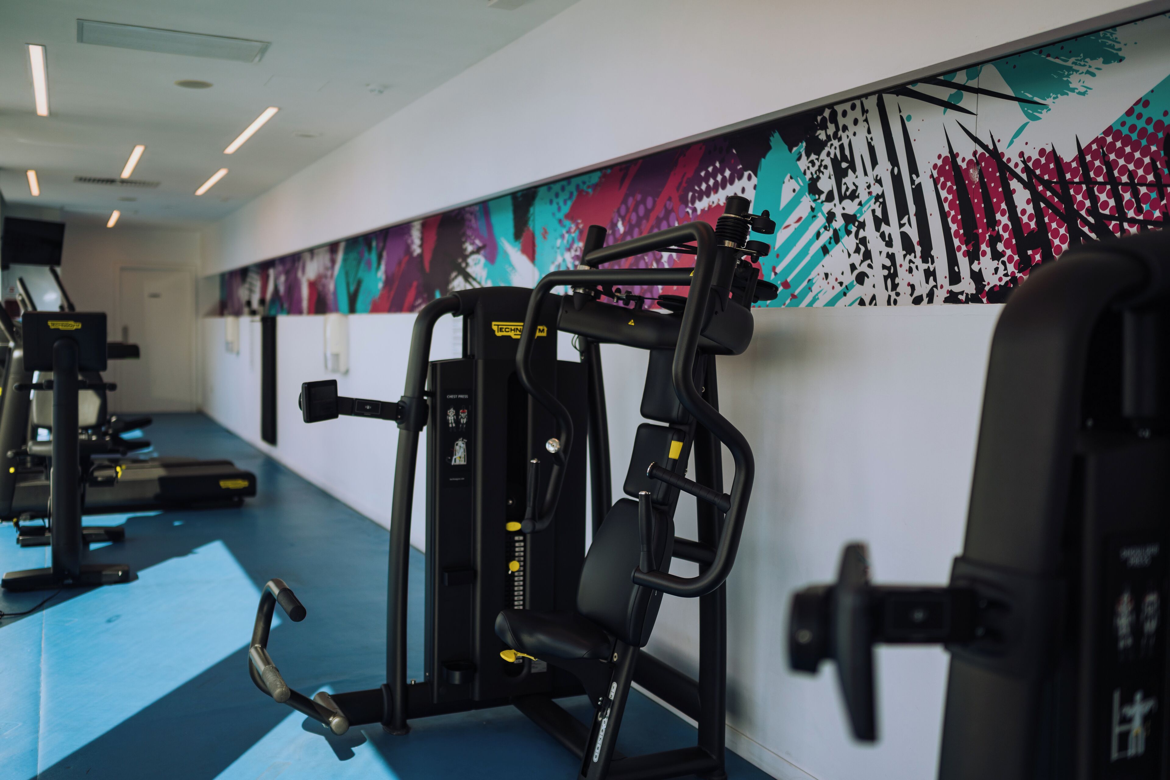 Un gimnasio con equipo de ejercicio y un mural colorido en la pared.