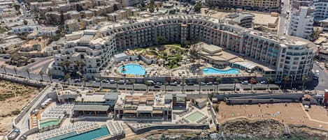 Un resort con varias piscinas, una zona de playa y vistas al mar.