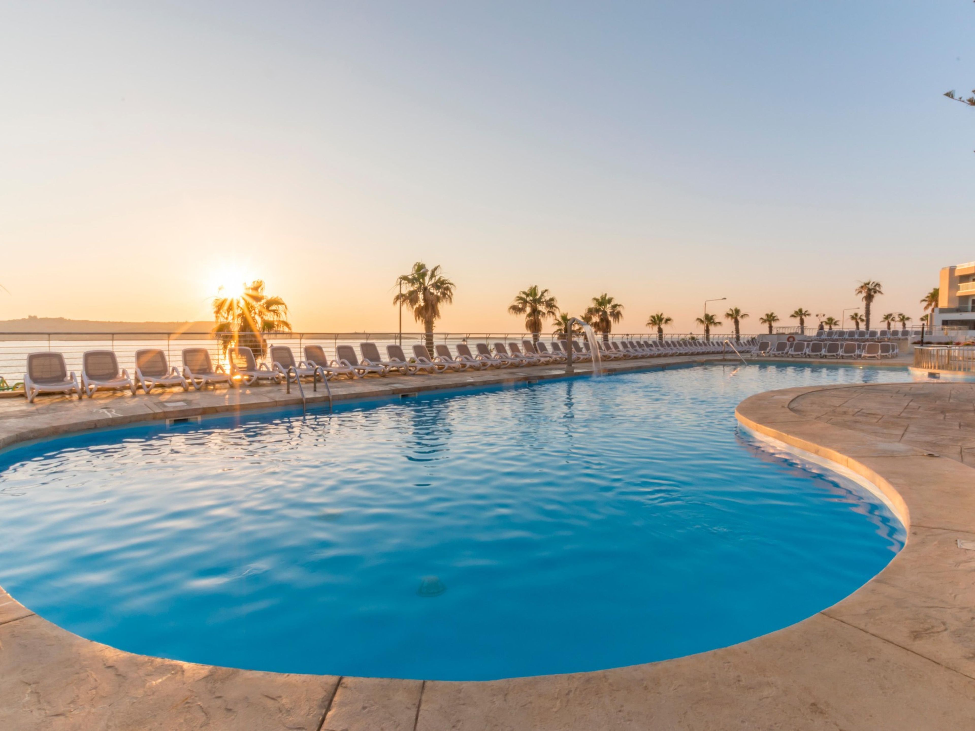 Una piscina con sillones de descanso y palmeras.