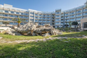 A modern hotel with a courtyard featuring rock formations, palm trees, and a paved walkway. - DoubleTree by Hilton Malta (St. Paul's Bay)