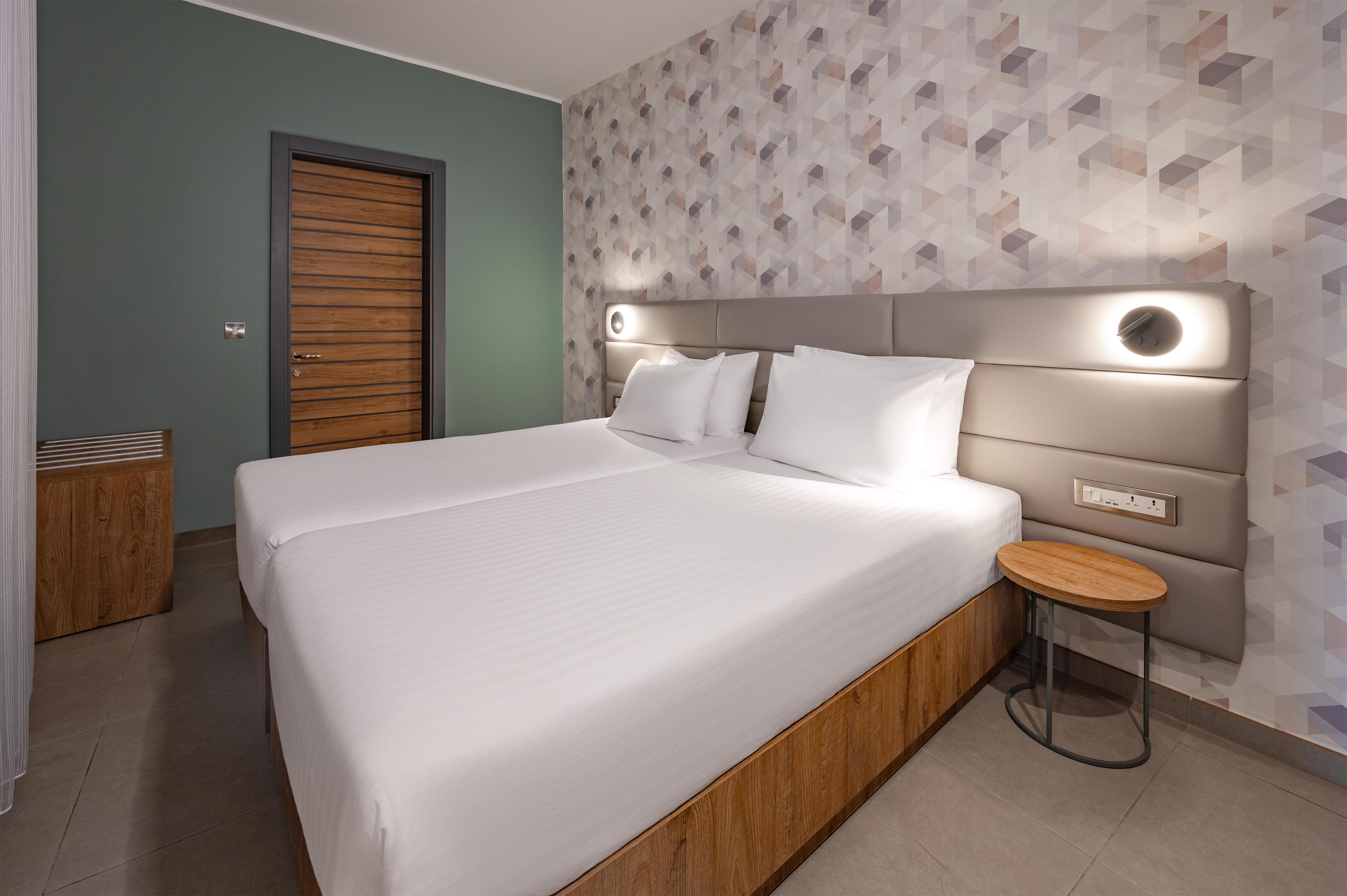 A modern hotel room with a large bed, a bedside table, and a wall-mounted light.