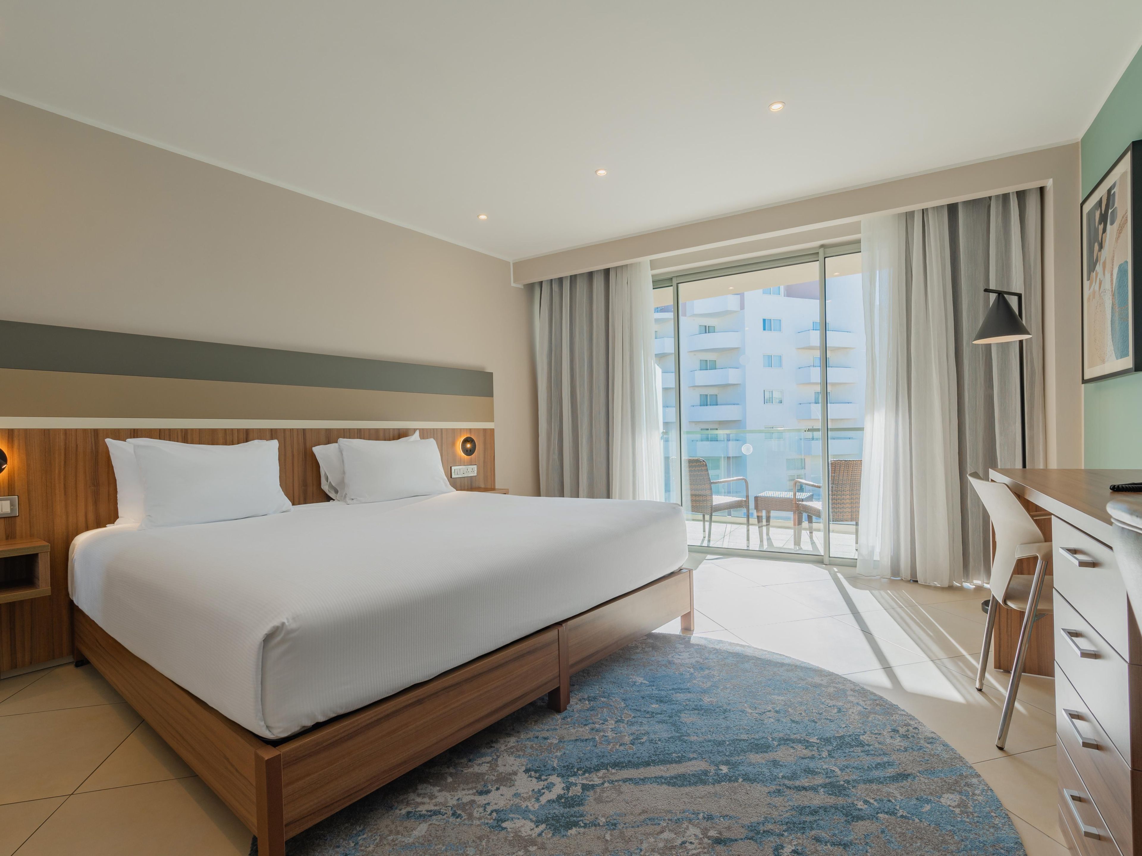 Una habitación de hotel moderna con una cama grande, un escritorio y un balcón con vistas a la ciudad.