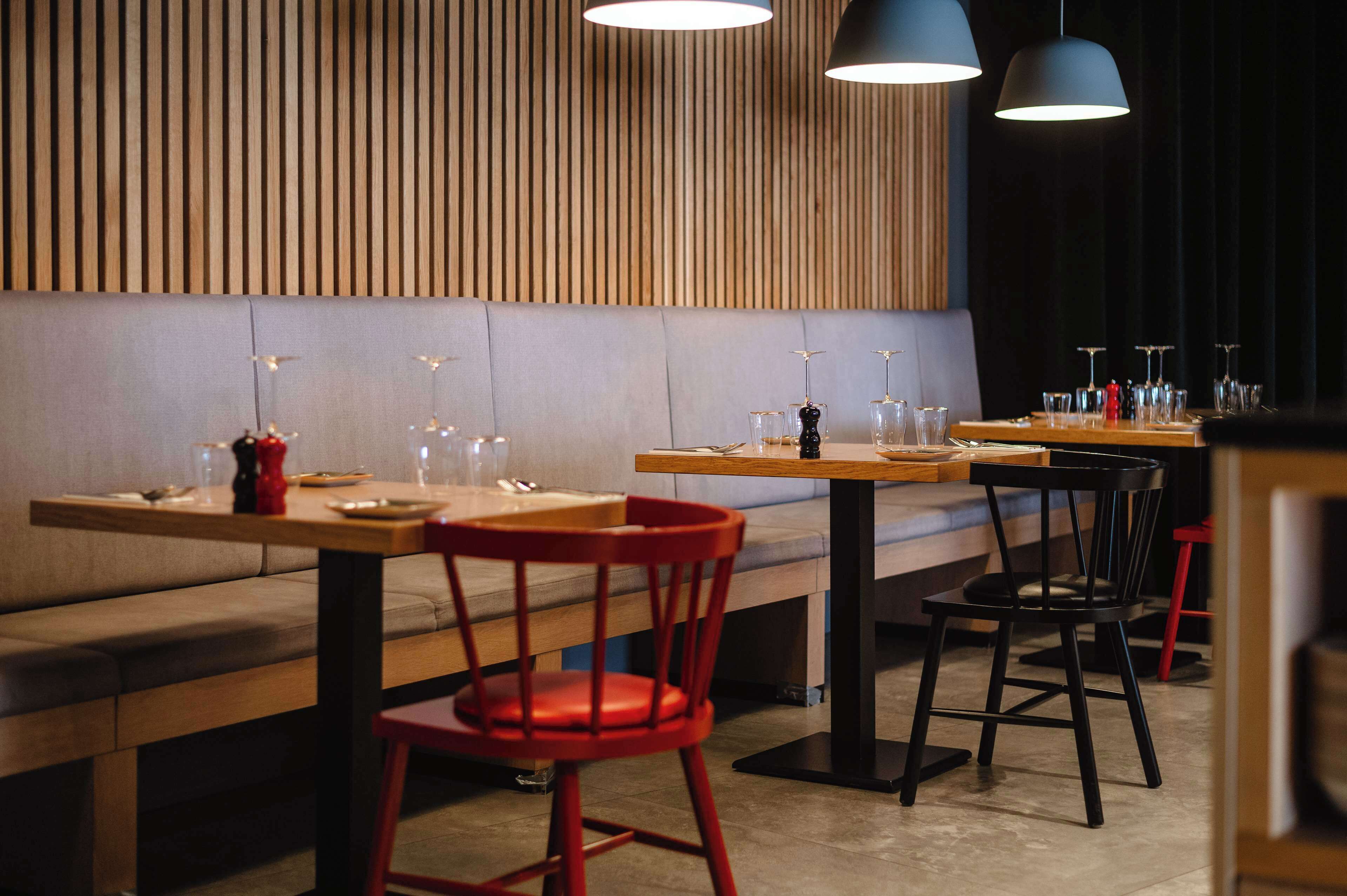 Interno di un ristorante con pareti in legno, illuminazione a sospensione e un mix di sedie rosse e nere.