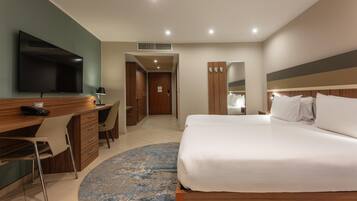 A hotel room with a bed, a desk with a chair, a television, and a bathroom visible through an open door.
