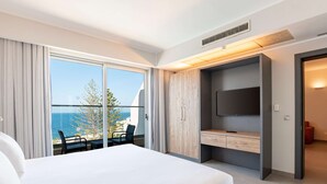 Una habitación de hotel moderna con una cama grande, televisión, escritorio y balcón con vista al mar.