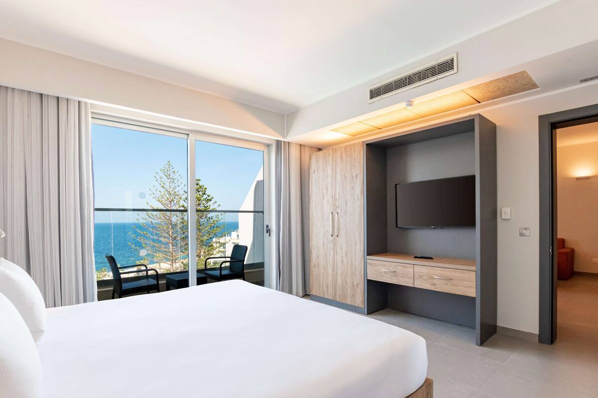 Una habitación de hotel moderna con una cama grande, televisión, escritorio y balcón con vista al mar.