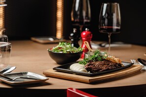 A dining table with a plate of food, a bowl of salad, and a wine glass. - DoubleTree by Hilton Malta (St. Paul's Bay)