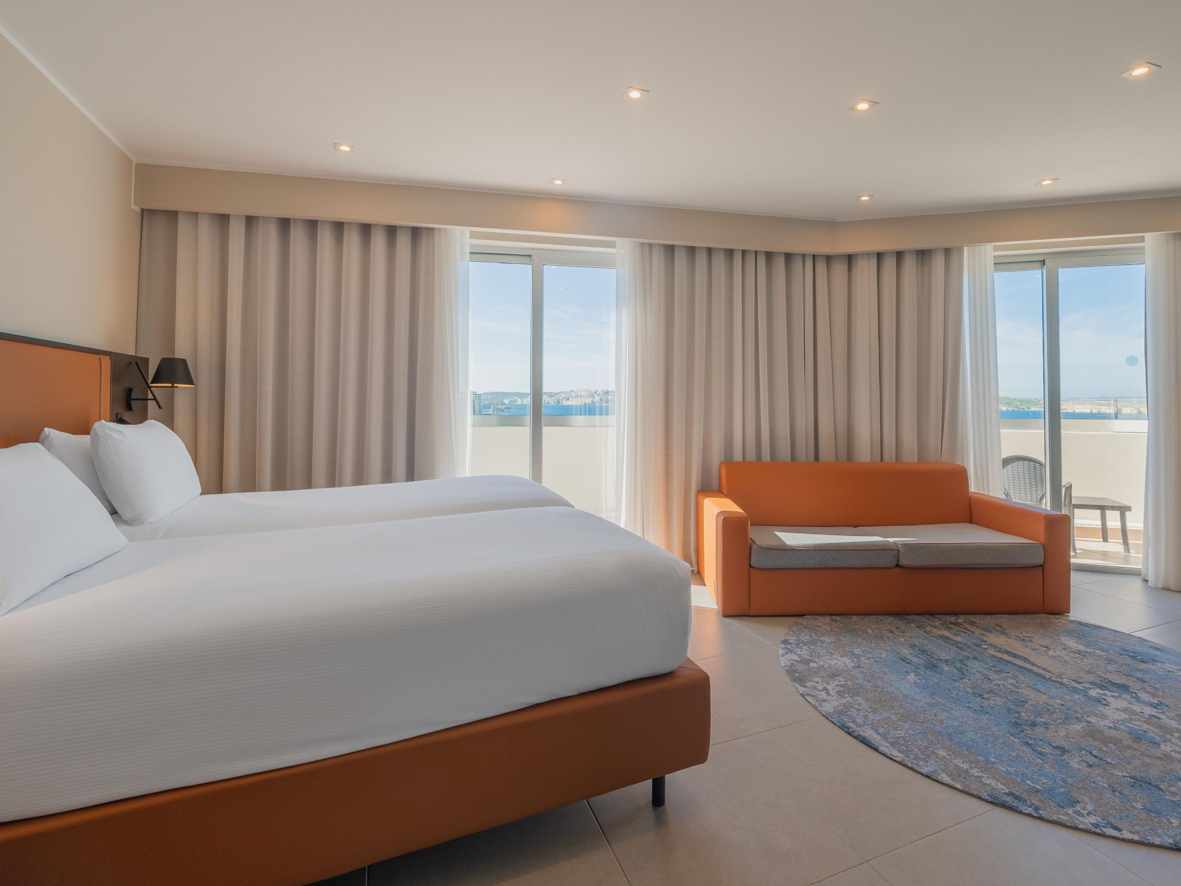 Habitación de hotel con una cama grande, un sofá, vista al mar y un balcón.