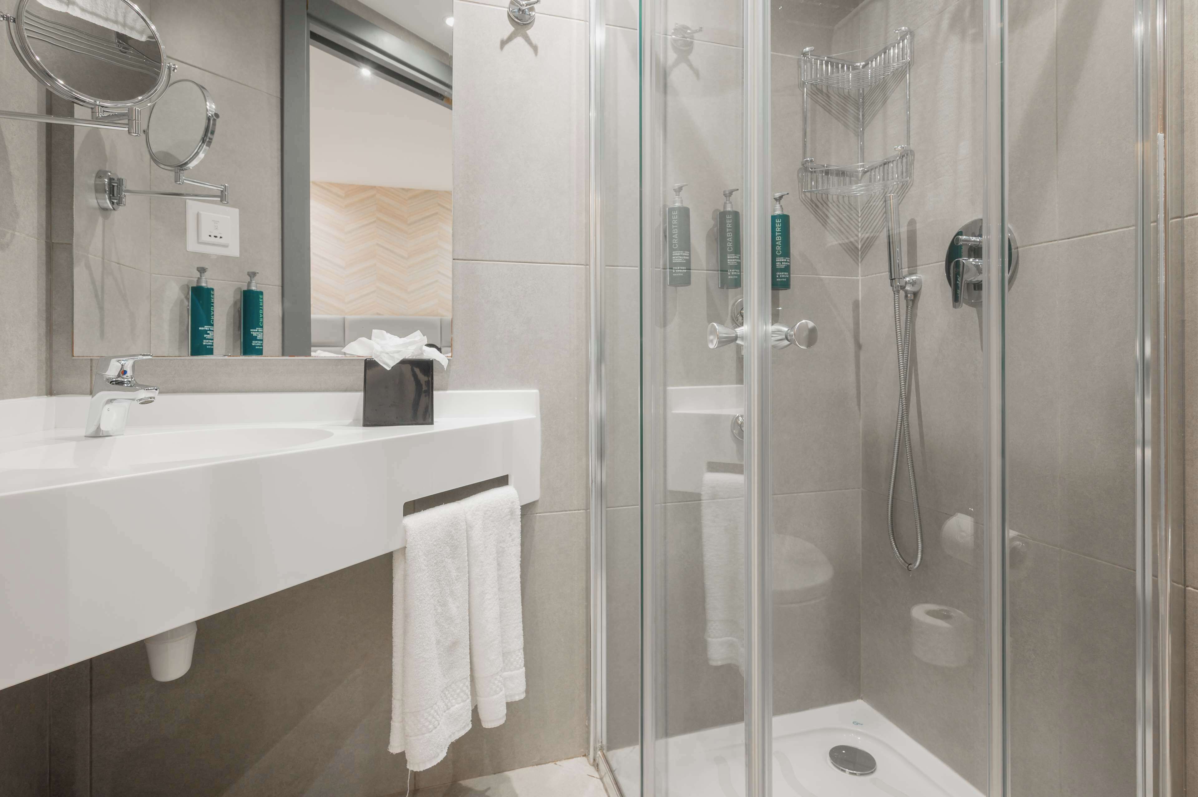 Een moderne badkamer met een douchecabine van glas, een witte wastafel en een spiegel.