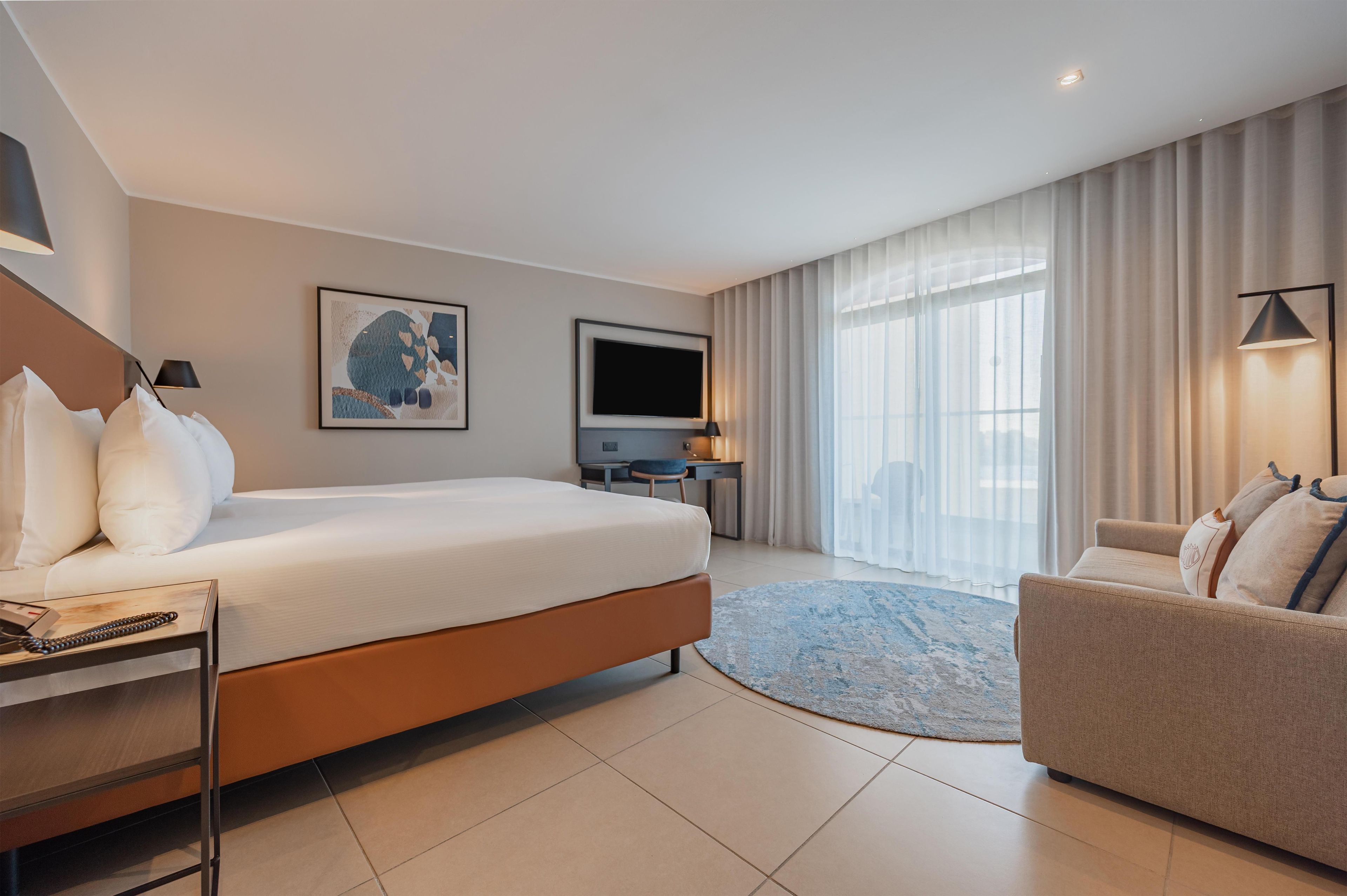 A hotel room with a bed, a desk, a television, and a sofa.