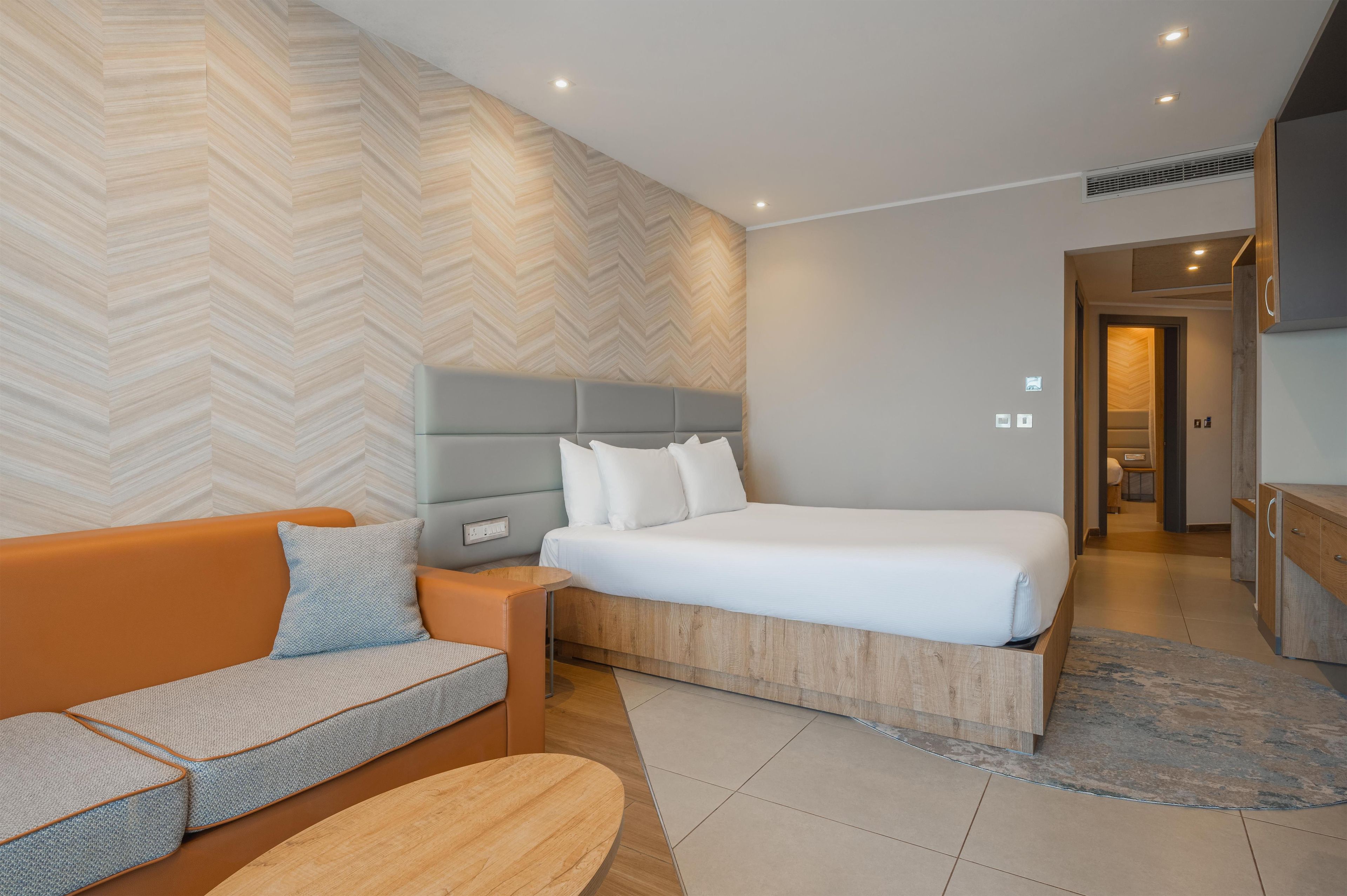 A modern bedroom with a bed, a sofa, a nightstand, and a wooden headboard.
