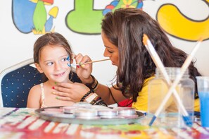 A child being painted by an adult at a table with art supplies. - DoubleTree by Hilton Malta (St. Paul's Bay)