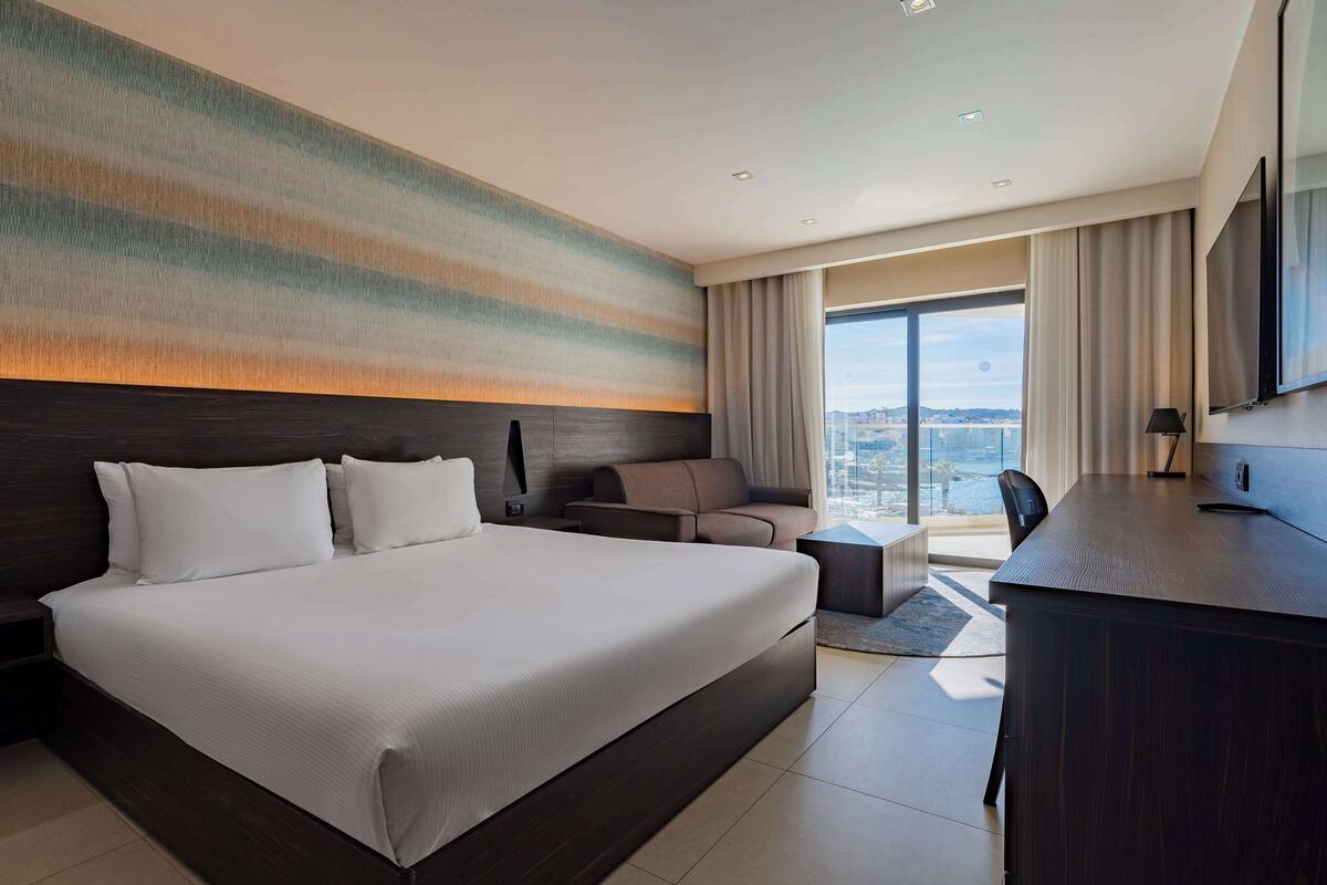 Una habitación de hotel moderna con una cama grande, un escritorio, un sofá y vistas a la ciudad.