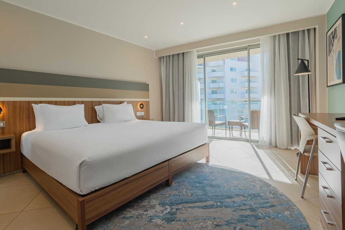 Una habitación de hotel moderna con una cama grande, un escritorio y un balcón con vistas a la ciudad.