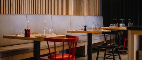 A restaurant interior with wooden paneling, tables, chairs, and hanging pendant lights.
