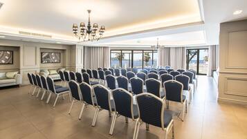 Un salón de conferencias con hileras de sillas, ventanas amplias y un candelabro.