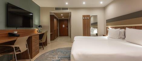 A hotel room with a bed, a desk with a chair, a television, and a bathroom visible through an open door.