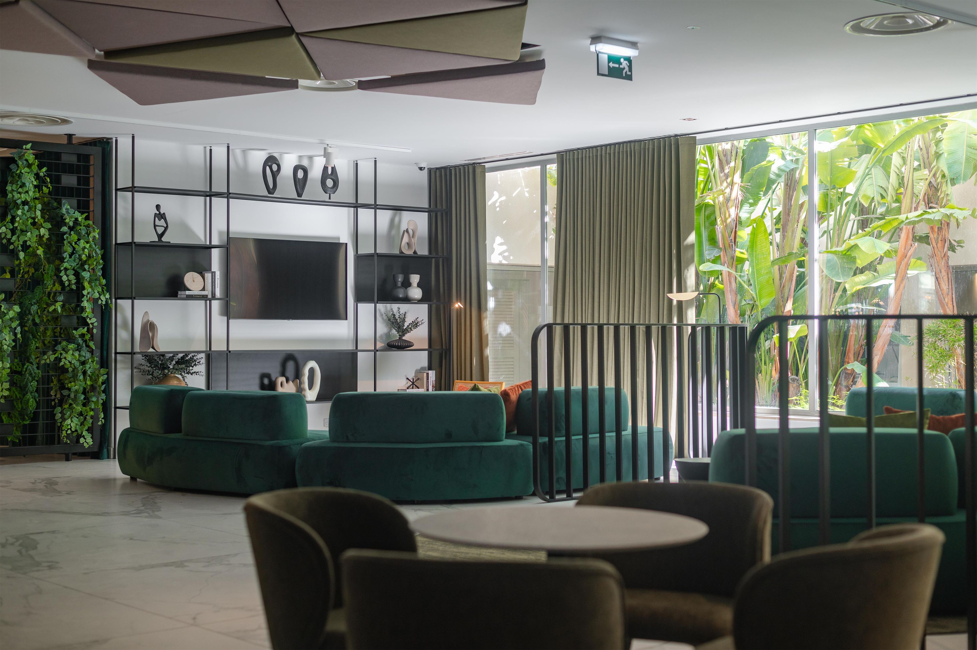 Un salon moderne avec un téléviseur à écran plat, des canapés verts et une grande fenêtre avec des rideaux.