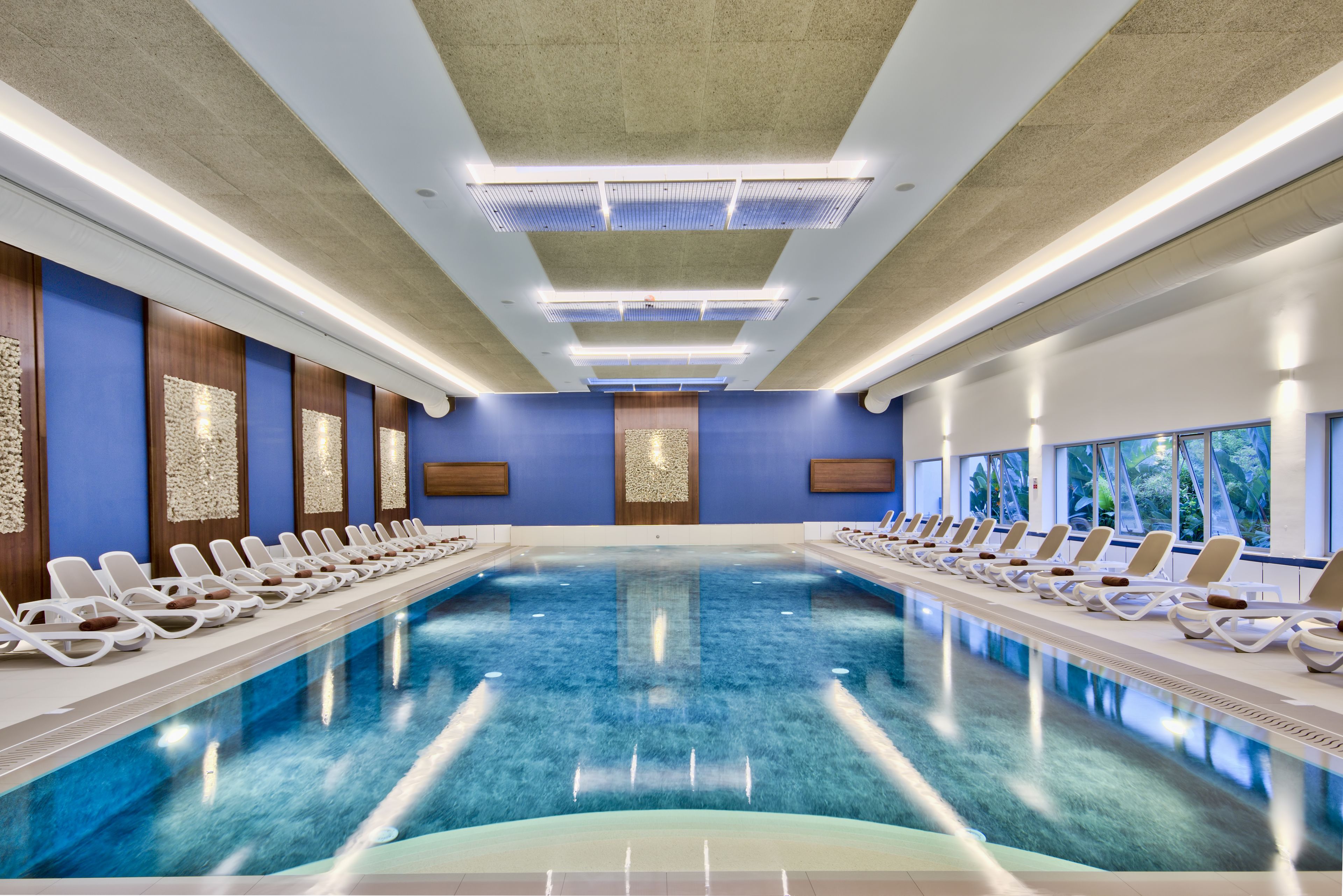 A large indoor swimming pool with lounge chairs and a modern ceiling design.