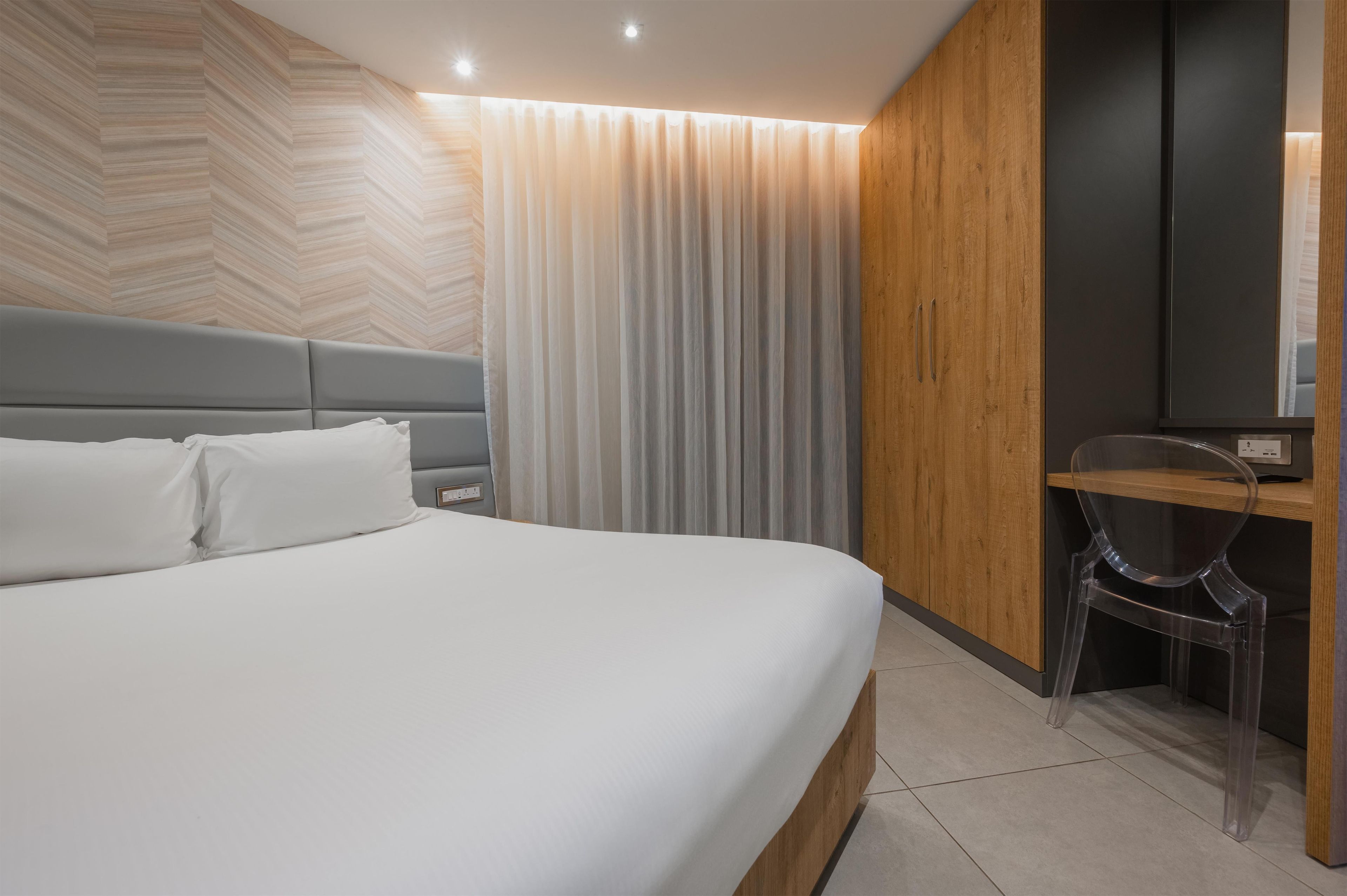 A modern hotel room with a large bed, a wooden panel wall, a desk, and a chair.