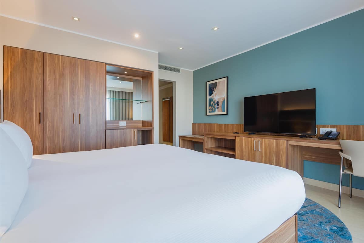 Una habitación de hotel moderna con una cama grande, un armario de madera, un escritorio con televisor de pantalla plana y una pared de acento azul.