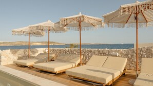 Zona de piscina con sillones reclinables y sombrillas, con vistas a una extensión de agua.