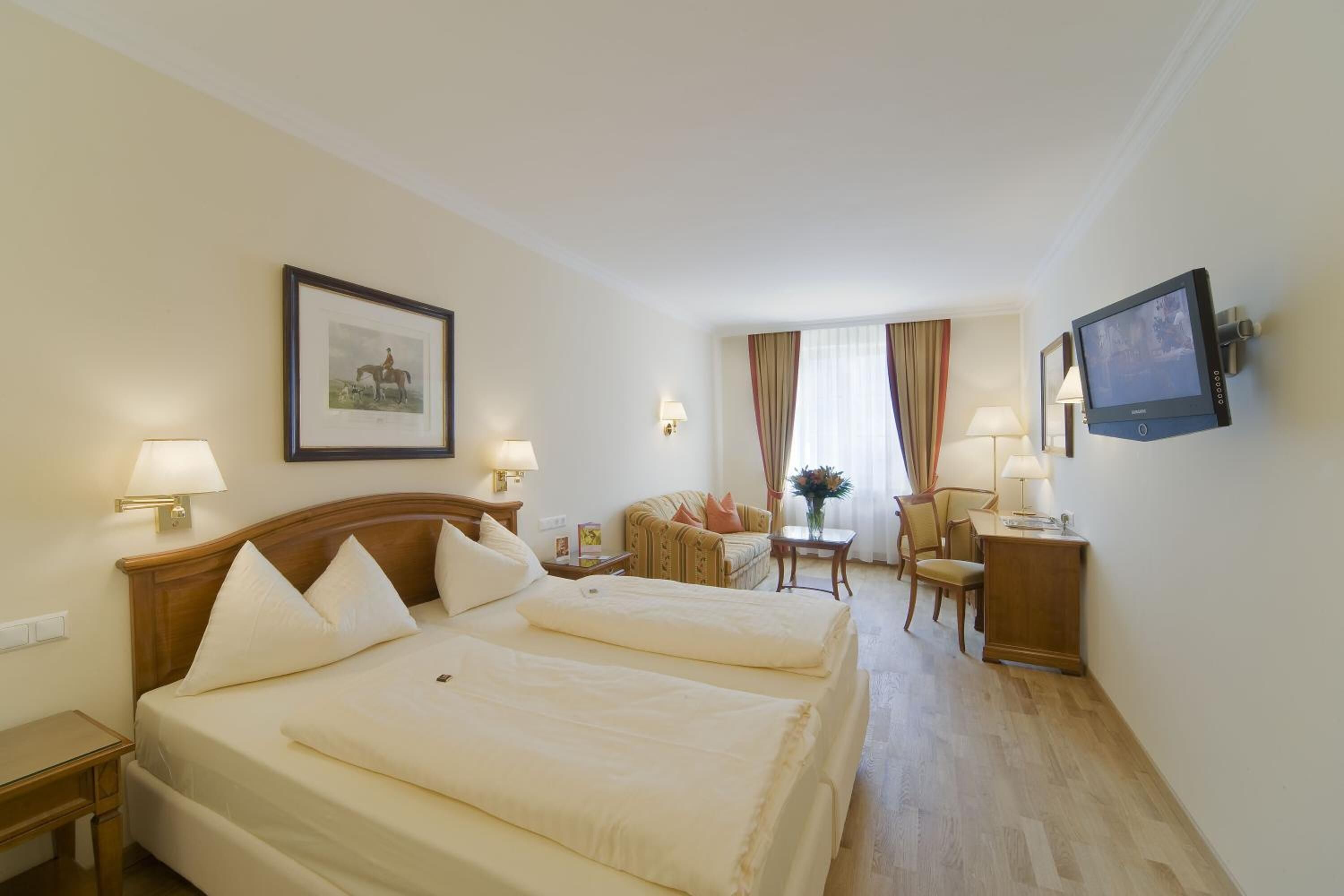 A hotel room with two beds, a desk, a chair, a TV, and a framed picture on the wall.