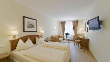 A hotel room with two beds, a desk, a chair, a TV, and a framed picture on the wall.