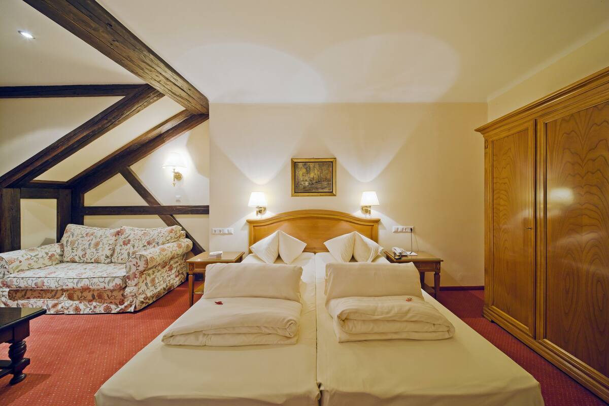 Habitación de hotel con dos camas, un sofá, un armario de madera y un cuadro en la pared.
