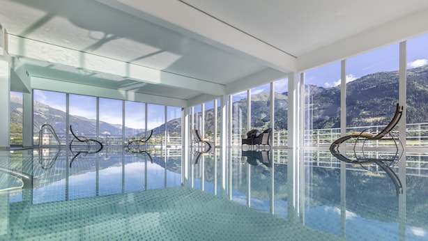 A spacious indoor swimming pool with clear glass walls, offering panoramic mountain views.