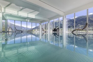 A spacious indoor swimming pool with clear glass walls, offering panoramic mountain views.
