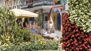 A hotel with multiple floors, balconies with flower boxes, and a garden area with various plants and flowers.