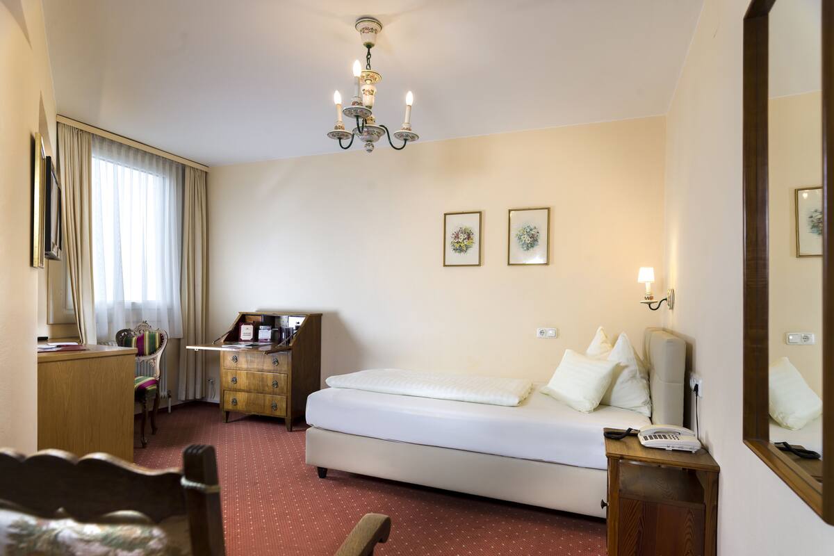 Habitación de hotel con cama, escritorio, silla, cómoda, espejo y candelabro.