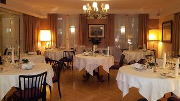Ein formeller Speisesaal mit mehreren gedeckten Tischen, einer Kronleuchter und gerahmten Kunstwerken an den Wänden.