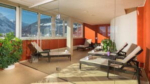 A modern lounge with glass walls, wicker furniture, and a mountain view.