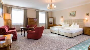 A hotel room with a bed, two red armchairs, a small table, a lamp, a dresser, and a mirror.