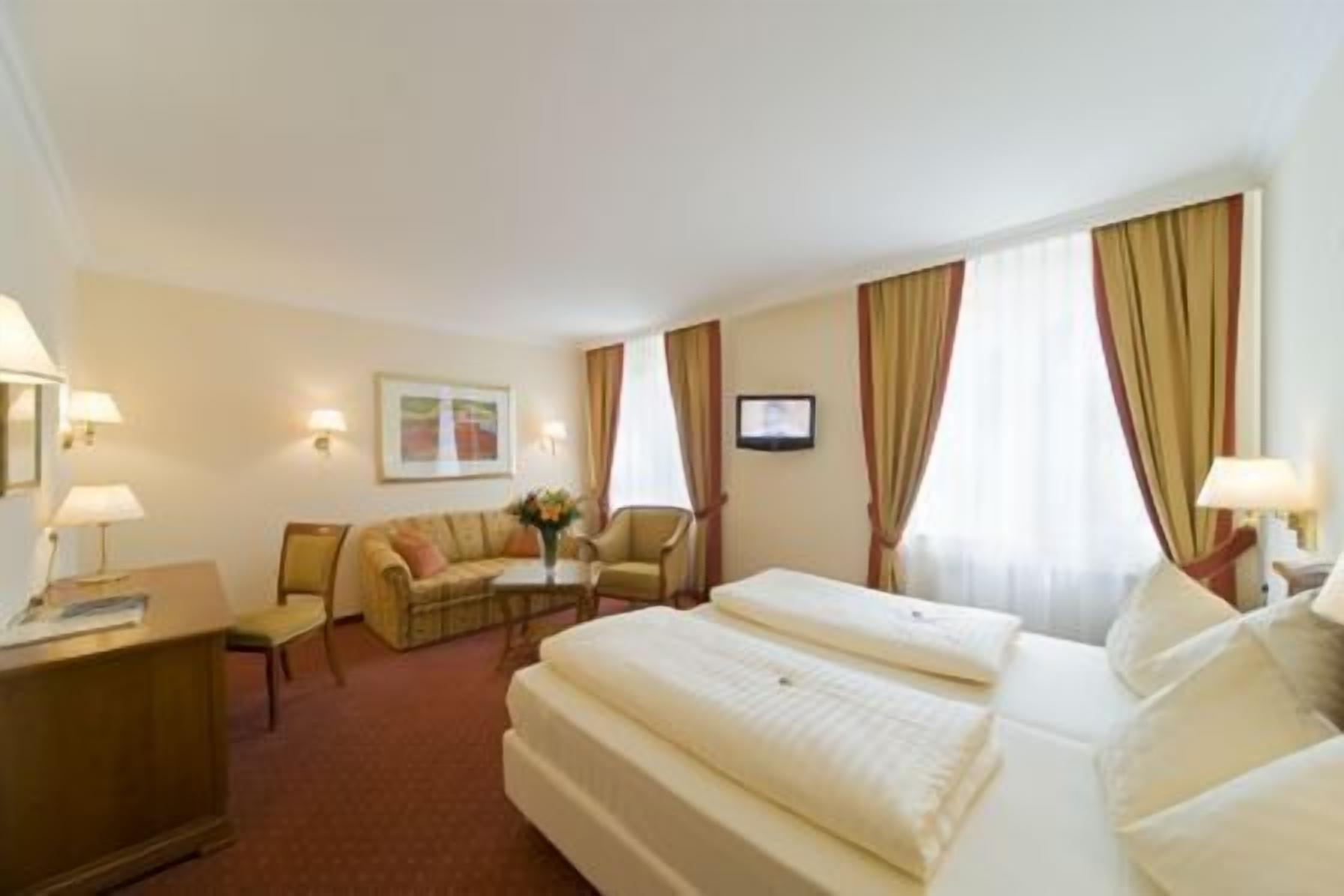 A hotel room with two beds, a desk, a chair, and a small table with a vase of flowers.