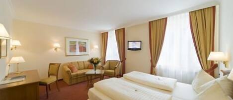 Habitación de hotel con dos camas, un escritorio, una silla y una mesita con un florero.