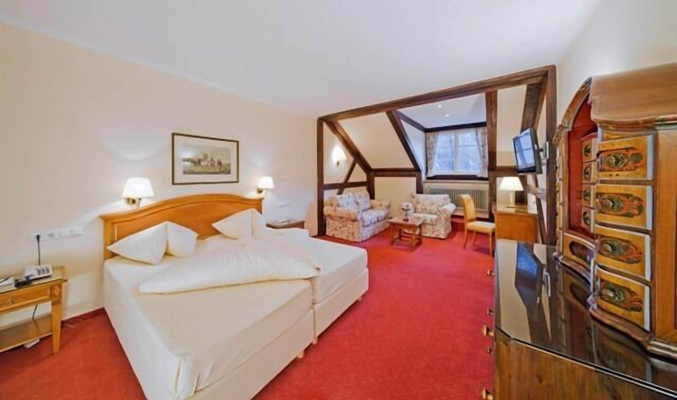 A hotel room with a bed, a desk, a chair, and a TV.