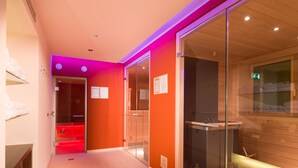 A modern hotel lobby with a glass partition, a reception desk, and a sauna visible through the glass.