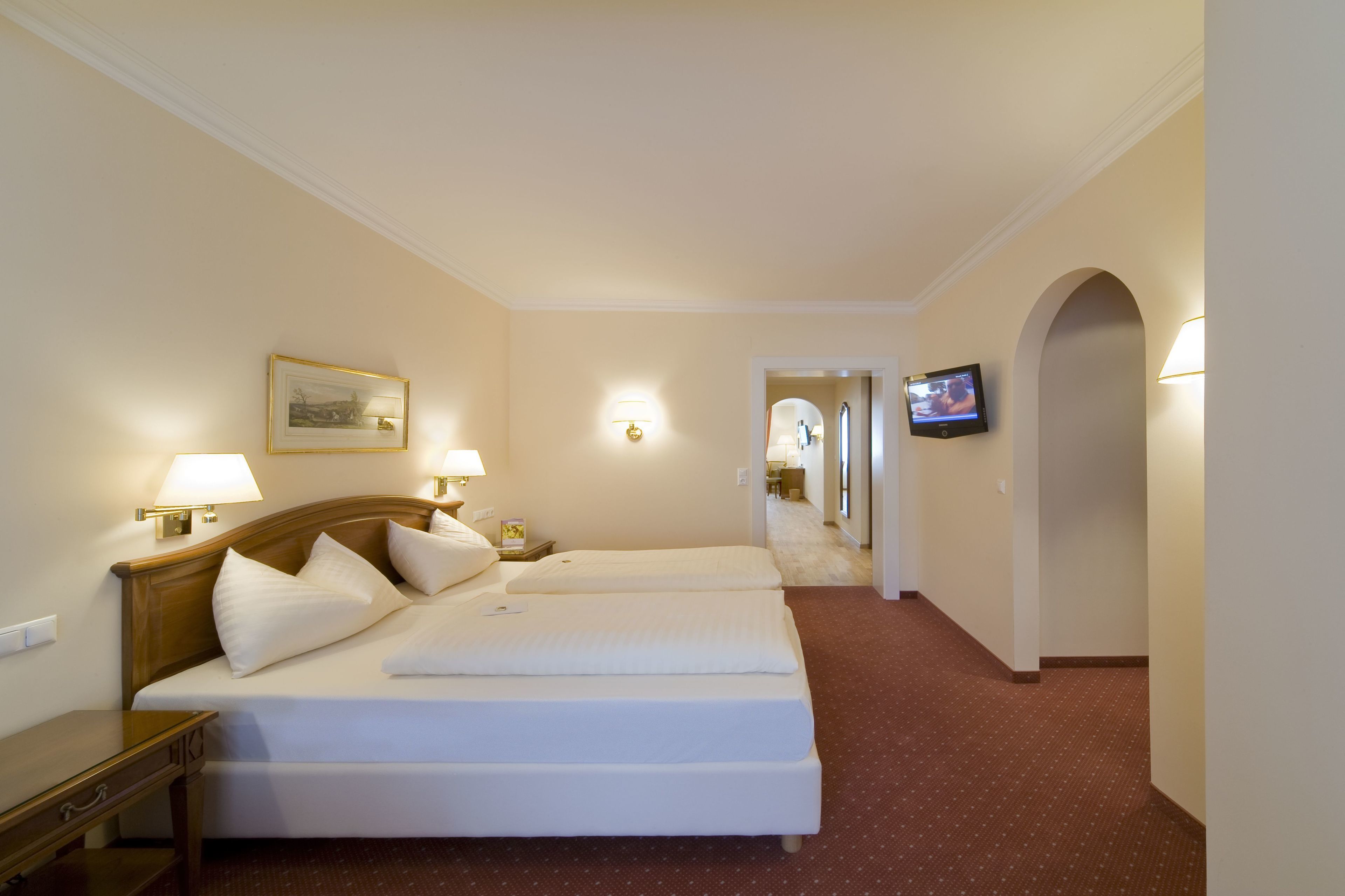 Een hotelkamer met twee bedden, een televisie en een gang naar een andere kamer.
