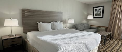 A hotel room with a large bed, two bedside tables, a nightstand, a desk, a chair, a lamp, and a picture on the wall.