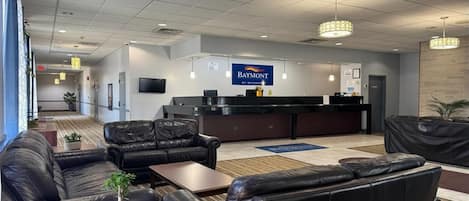 A hotel lobby with leather sofas, a reception desk, a television, and a sign for 'Baymont.'
