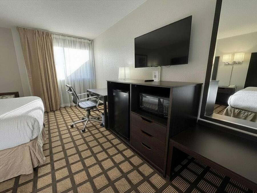 A hotel room with a bed, desk, chair, television, and a mirror.