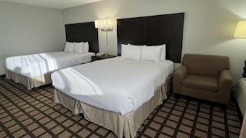 A hotel room with two beds, a chair, a nightstand, and a lamp.