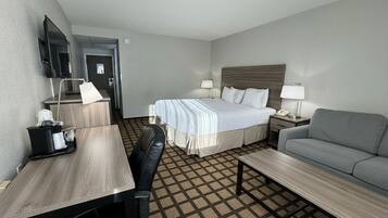 Una habitación de hotel con cama, escritorio, silla, sofá y televisor montado en la pared.