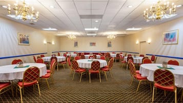 A conference room with round tables, red chairs, and chandeliers.
