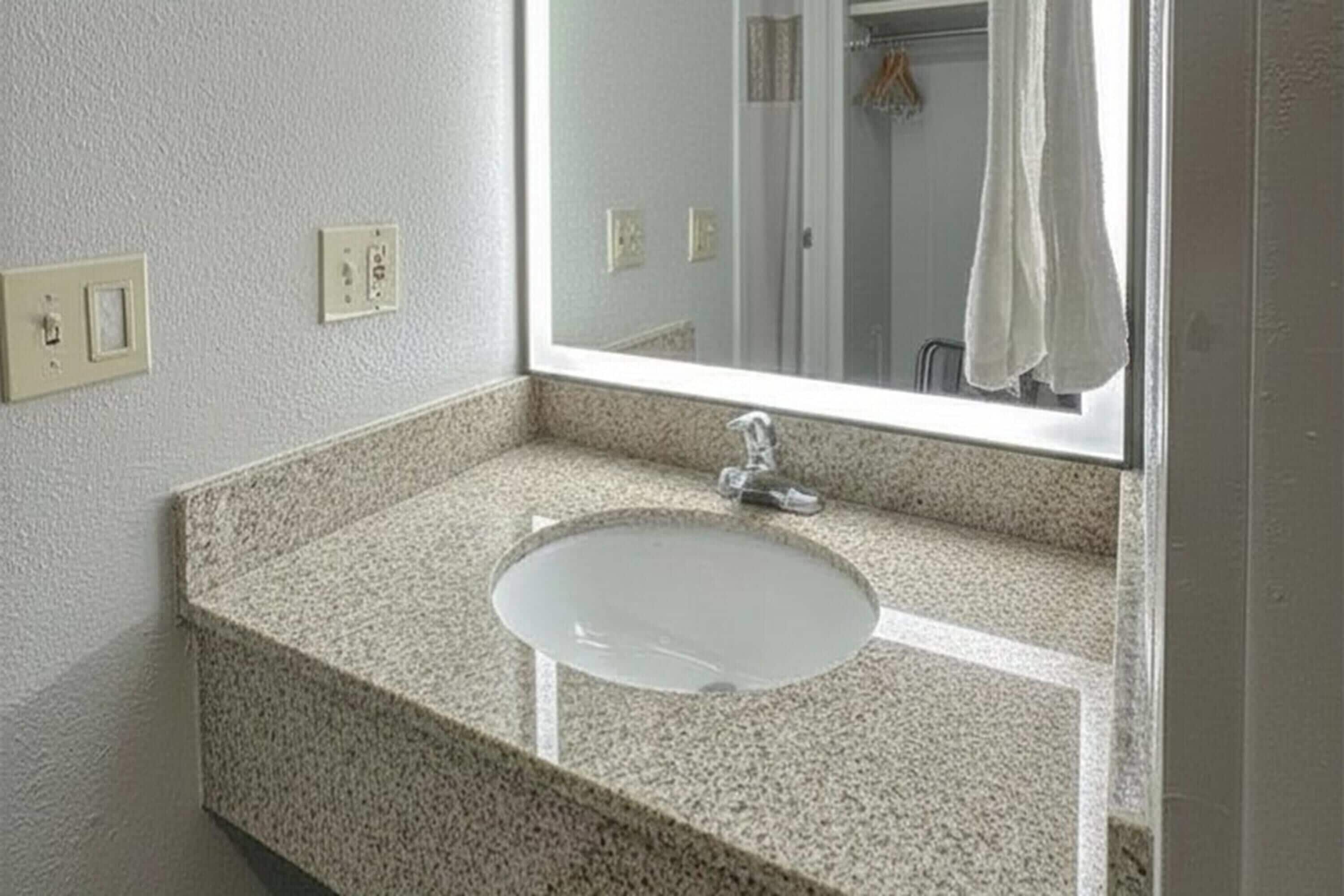 Un baño con encimera de granito, un lavamanos blanco y un espejo encima.